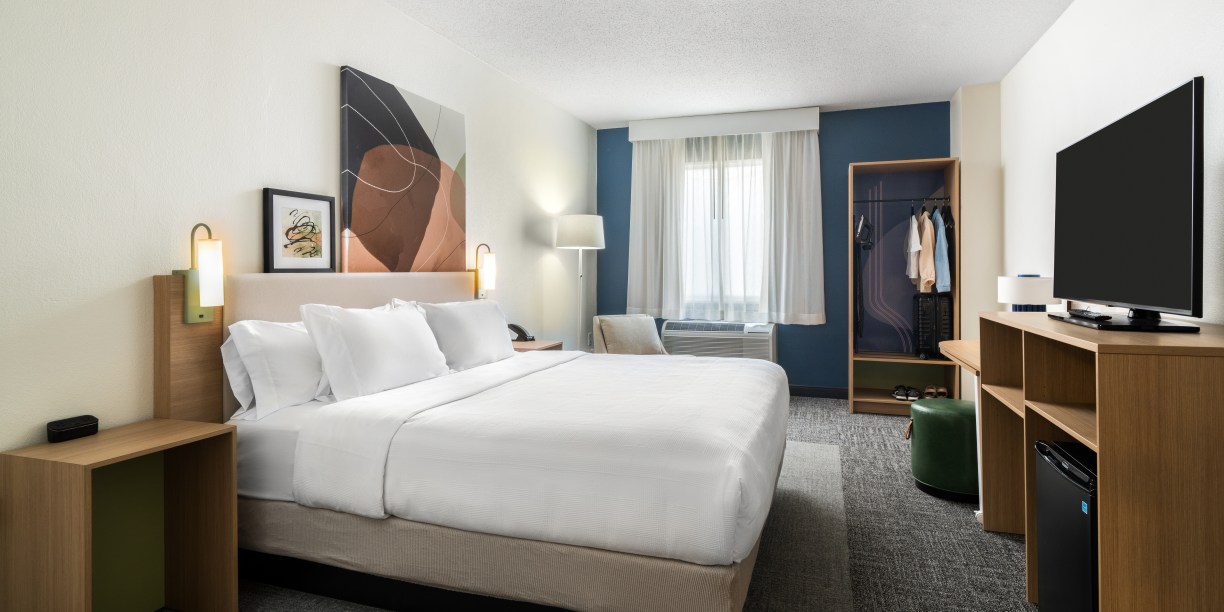 1 king bed in hotel guestroom with closet, tv and fridge at Spark by Hilton a new hotel brand