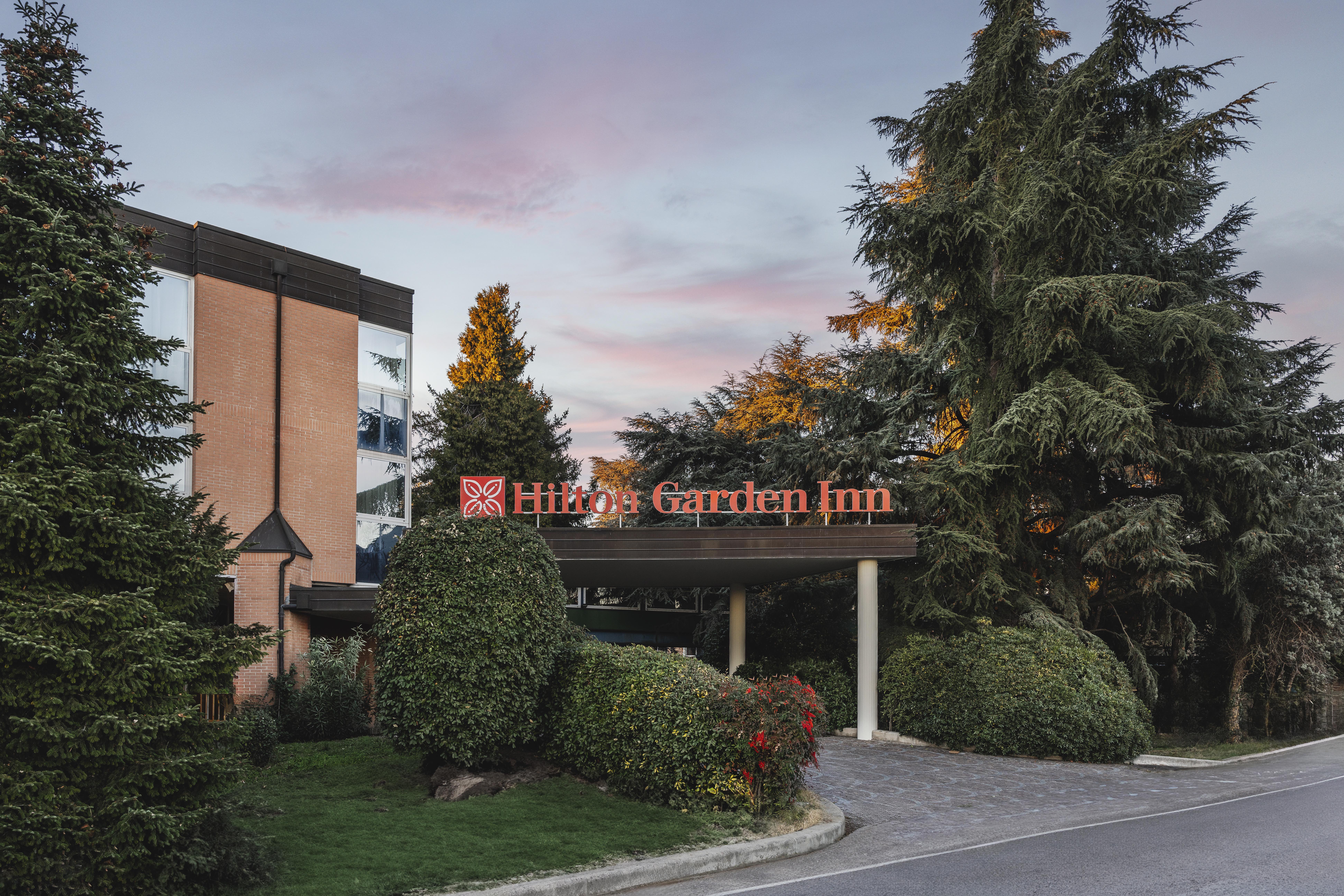 Hilton Garden Inn Bologna North Exterior, signage, trees, bushes, driveway, at sunset