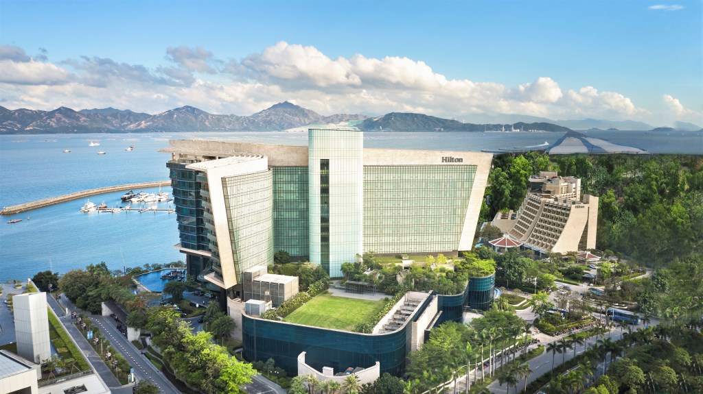 Hilton Shenzhen Shekou Nanhai exterior aerial photo, mountain and ocean view in the distance, palm trees and roadways in the foreground