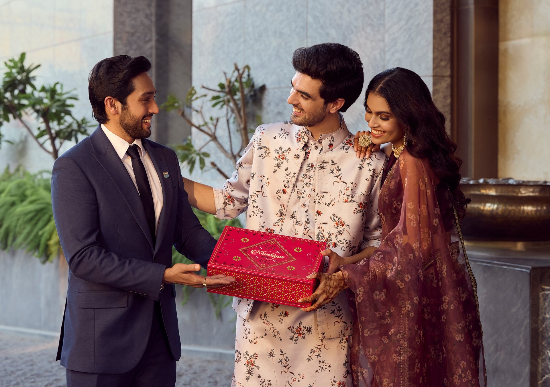 man and woman receiving red and gold gift box from man in a suit