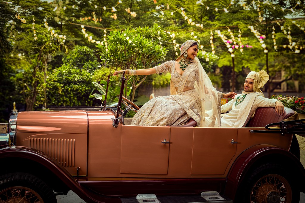 Man and woman in Indian wedding attire sitting in an antique orange car