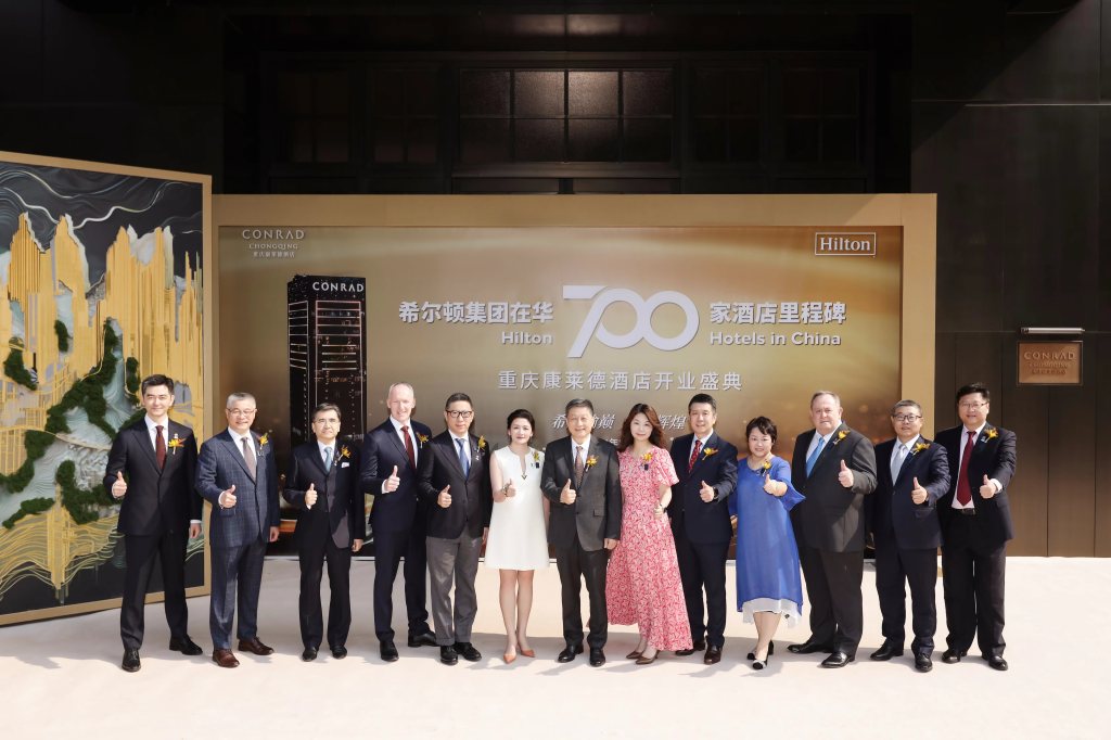 Group of people giving a thumbs up in front of a 700 Hilton hotels in China banner