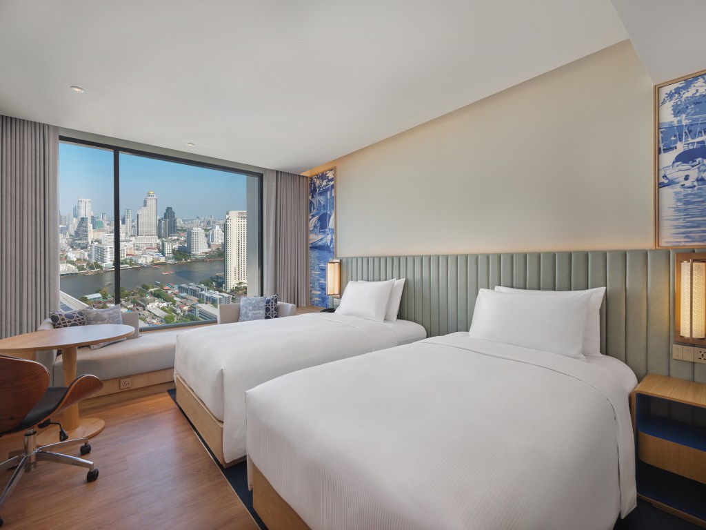 two twin beds with white bedding and large window overlooking the river and Bangkok skyline at Hilton Garden Inn Bangkok Riverside