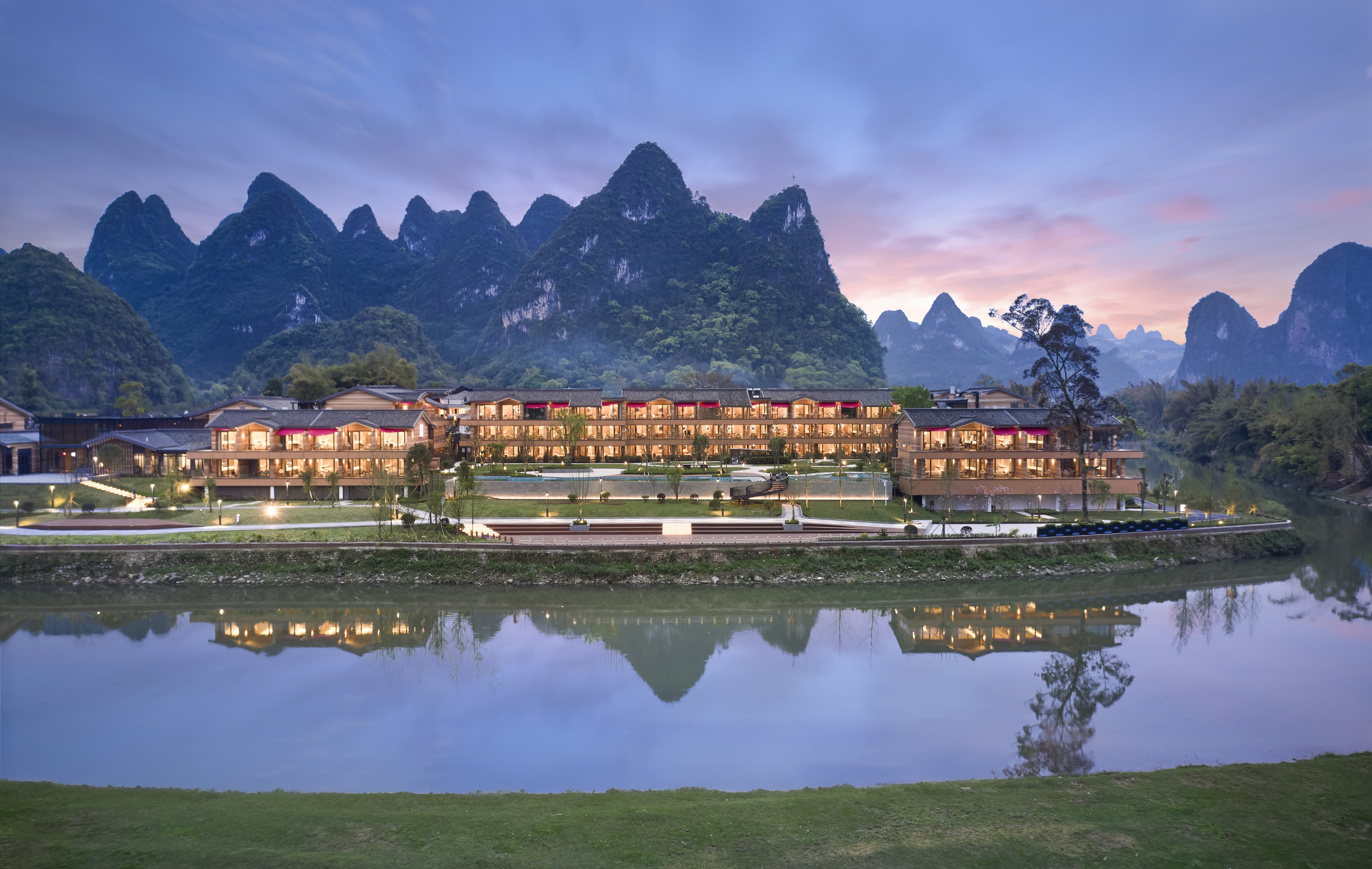 Hilton Garden Inn Guilin Yangshuo - Exterior, water front hotel with mountains behind at dusk