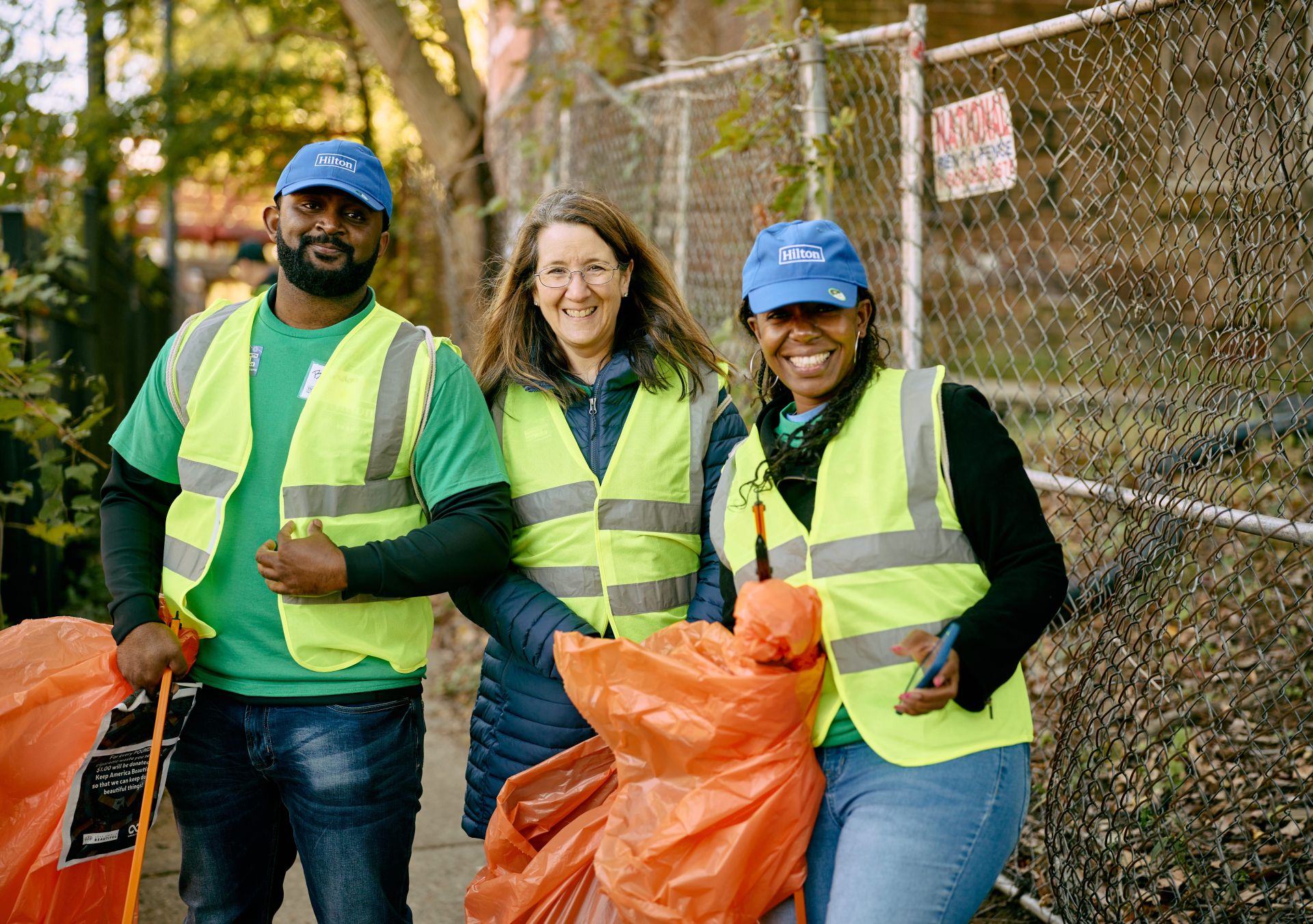 three volunteers wearing Hilton blue caps, safety vests and holing orange garbage bags