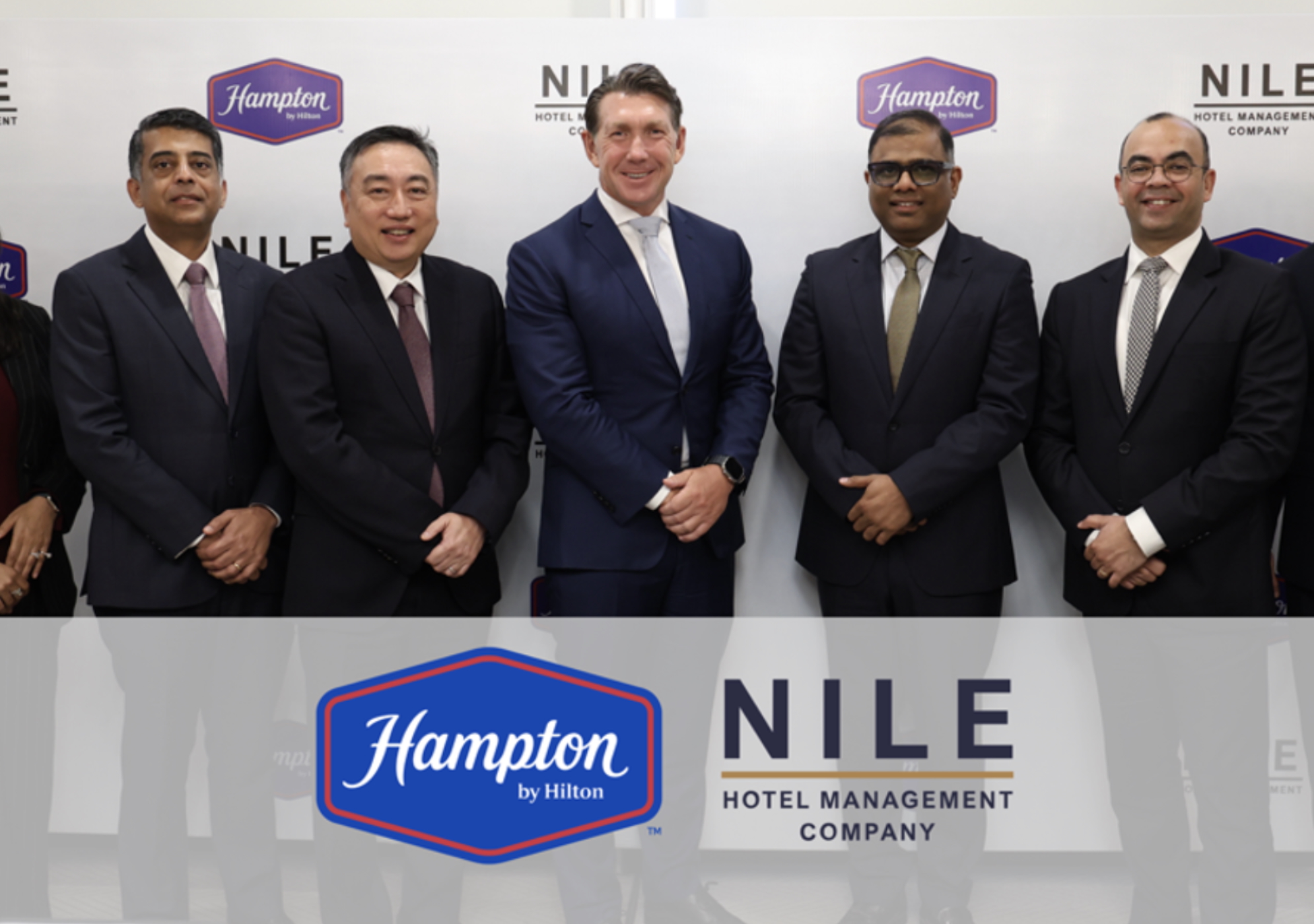 people standing and smiling in front of Hampton and NILE Hotel Management Company logo backdrop at the Hampton by Hilton and NILE Hospitality Signing Ceremony