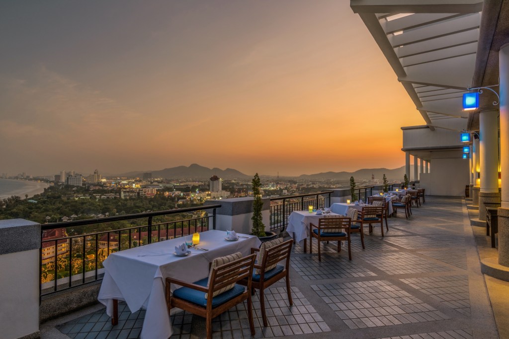 Hilton Hua Hin Resort &amp; Spa Thailand, dinner with a view, dining area, blue outdoor lights, white table setting, blue seat cushions, city view, sunset