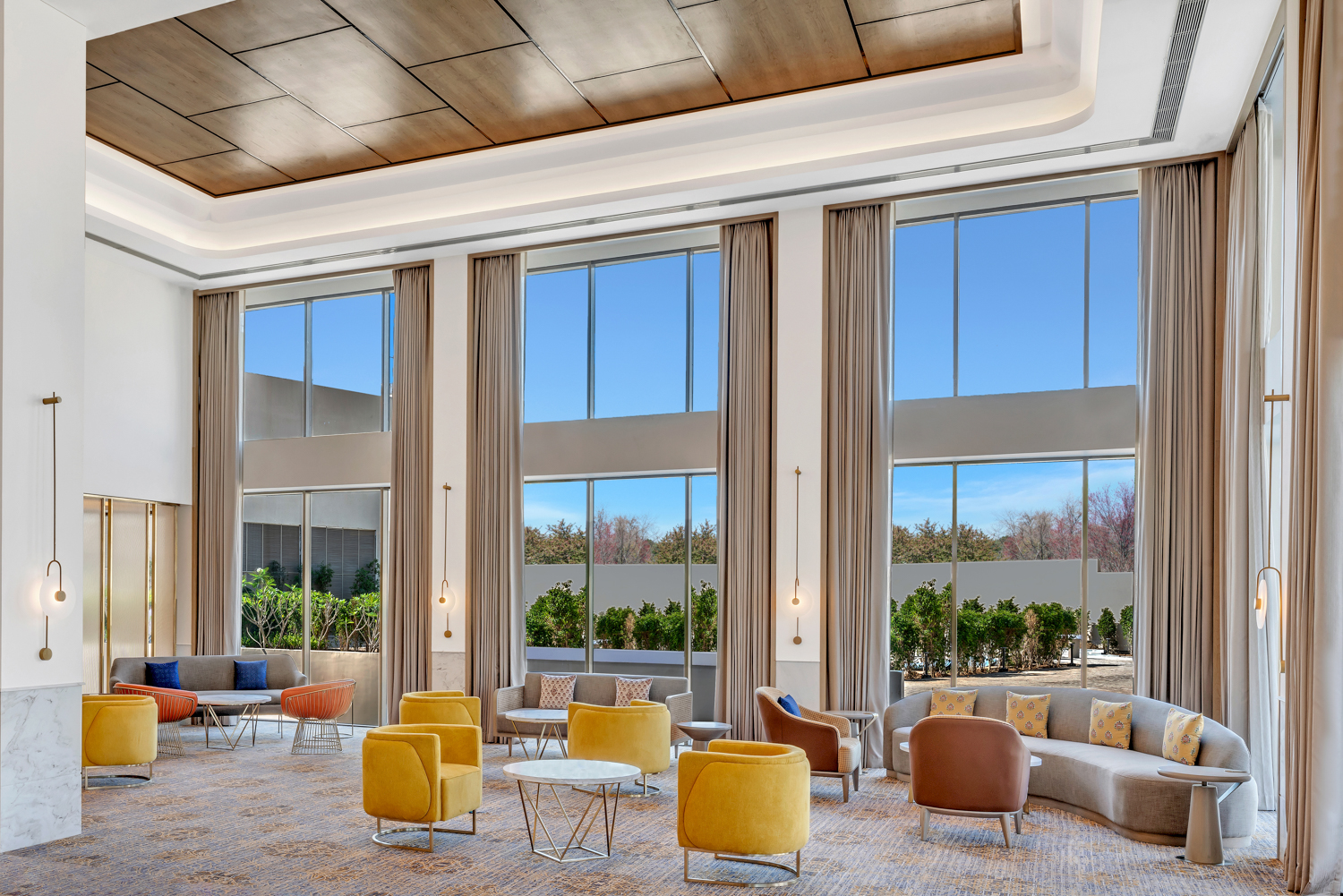 Lobby that has high ceilings with wood paneling and large windows with curtains and walls with marble paneling and wall sconce lighting, seating area with accent chairs and couches with end tables and coffee tables