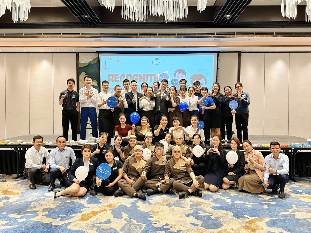 Hilton Named #1 Best Workplace in Vietnam - Hilton Da Nang - large group photo of team members posing with signs on a stage