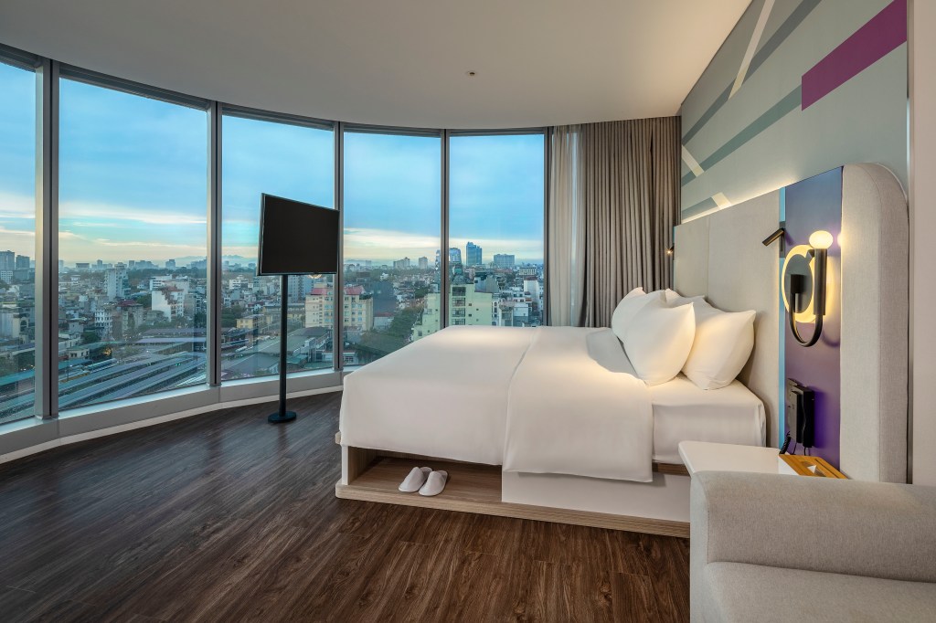 Tru by Hilton Hanoi Station King Room with Sofa Bed, king bed with white bedding overlooking floor to ceiling windows with views of the city