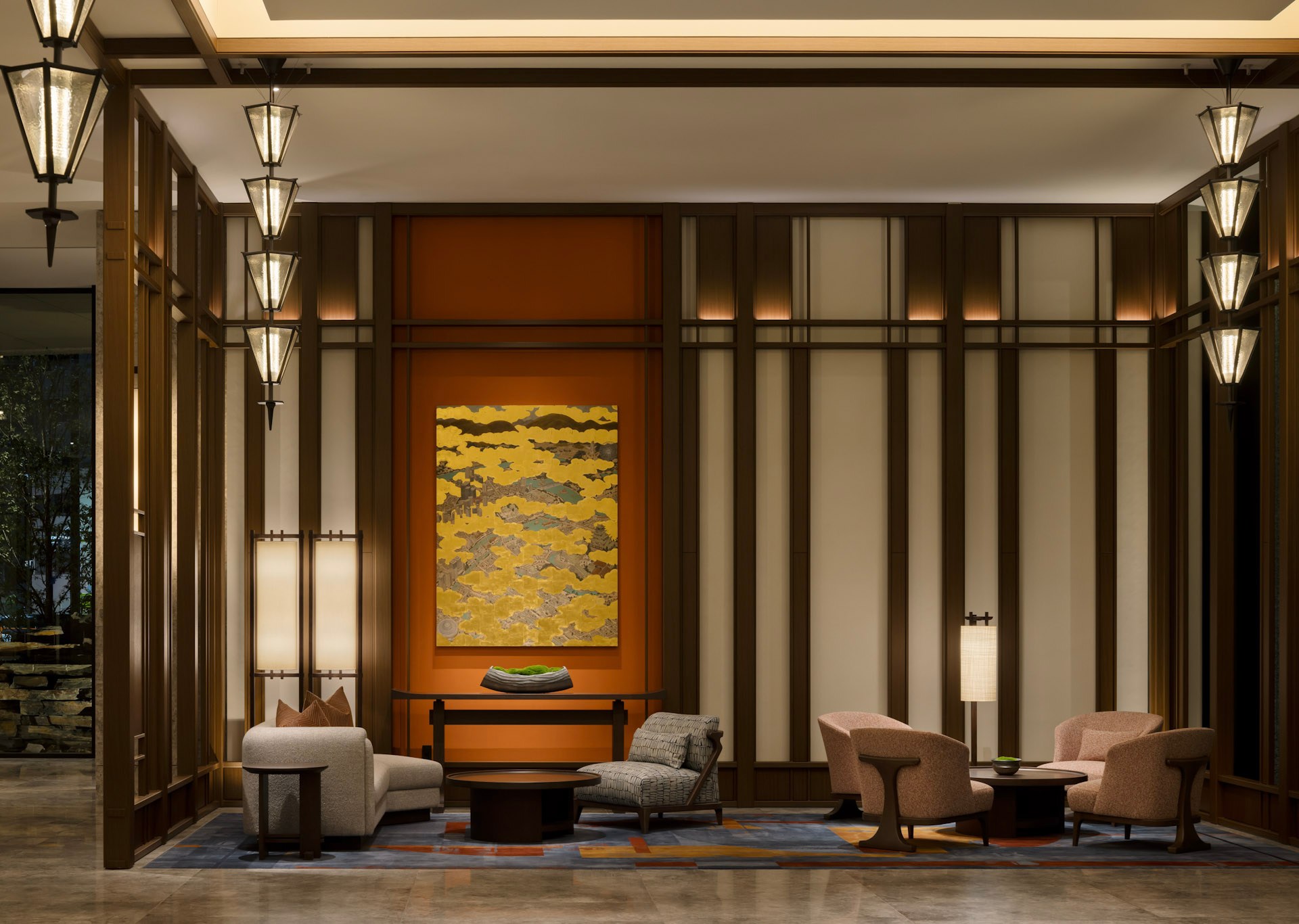 Contemporary hotel lounge with comfortable seating, vertical wood paneling, and a golden-hued abstract painting. Waldorf Astoria Osaka - Grand Entrance - Lobby. Hilton