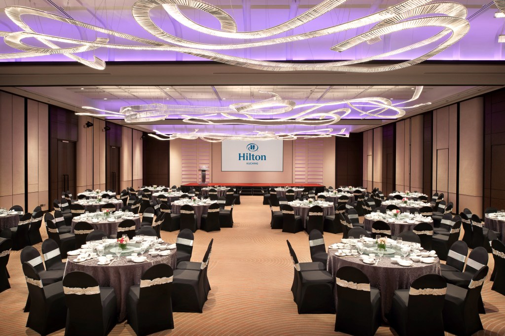 Large ballroom with tables and chairs and ceiling lighting fixture with purple overhead lighting