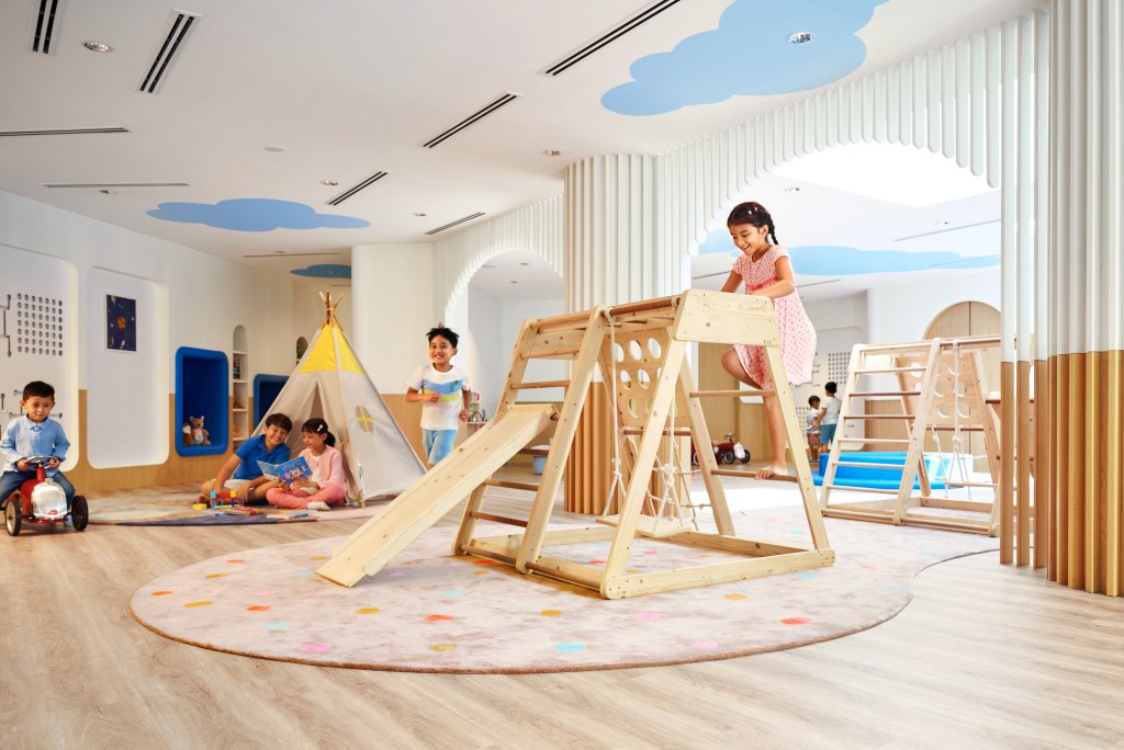 Hilton Kuching Kids Club with wooden play scapes with swings and tents and blue painted clouds on the ceiling and ridable toys