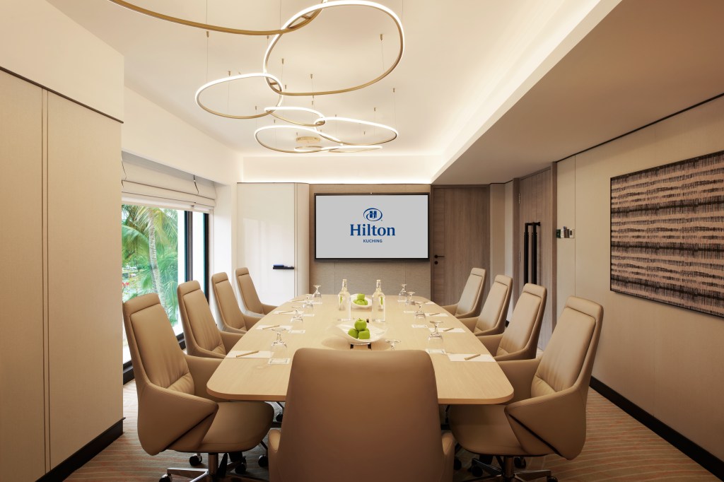 Conference/meeting room with long table and  large swivel chairs, television, windows, overhead lighting fixture