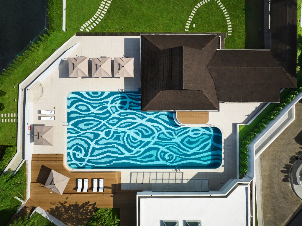 Hilton Kuching aerial view of pool with a unique design on the floor with lounge seating on all sides and beige umbrellas