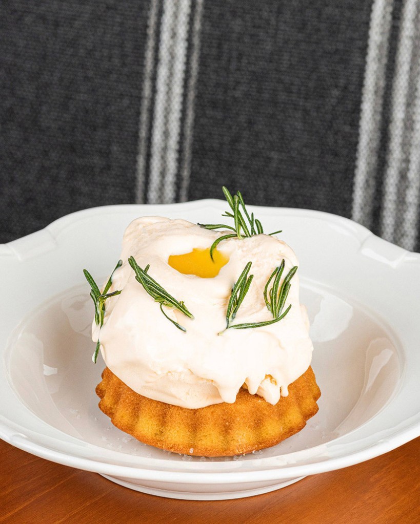 A delicate rosemary olive oil cake topped with creamy frosting, a drizzle of golden olive oil, and garnished with fresh rosemary sprigs.