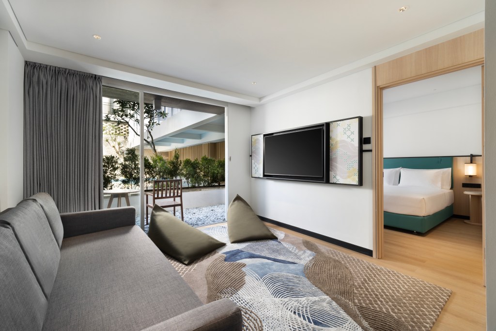 A living area in the King Deluxe Family Room with couch and floor cushions, overlooking a balcony.