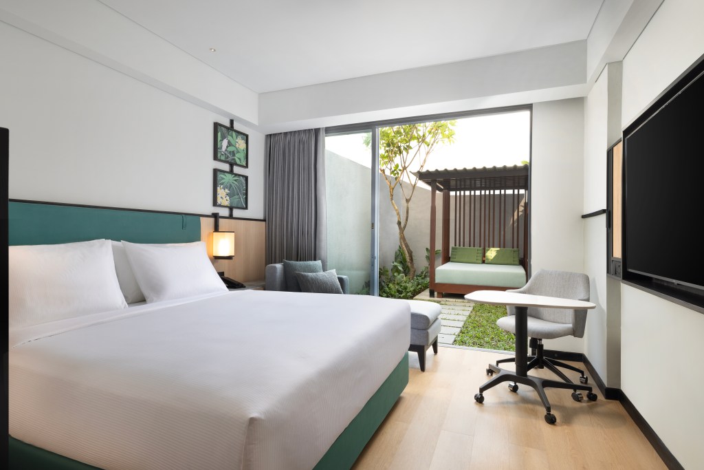 A room at the Hilton Garden Inn Bali Nusa Dua with King bed, chaise, and chair looking out on a terrace with an outdoor bed.