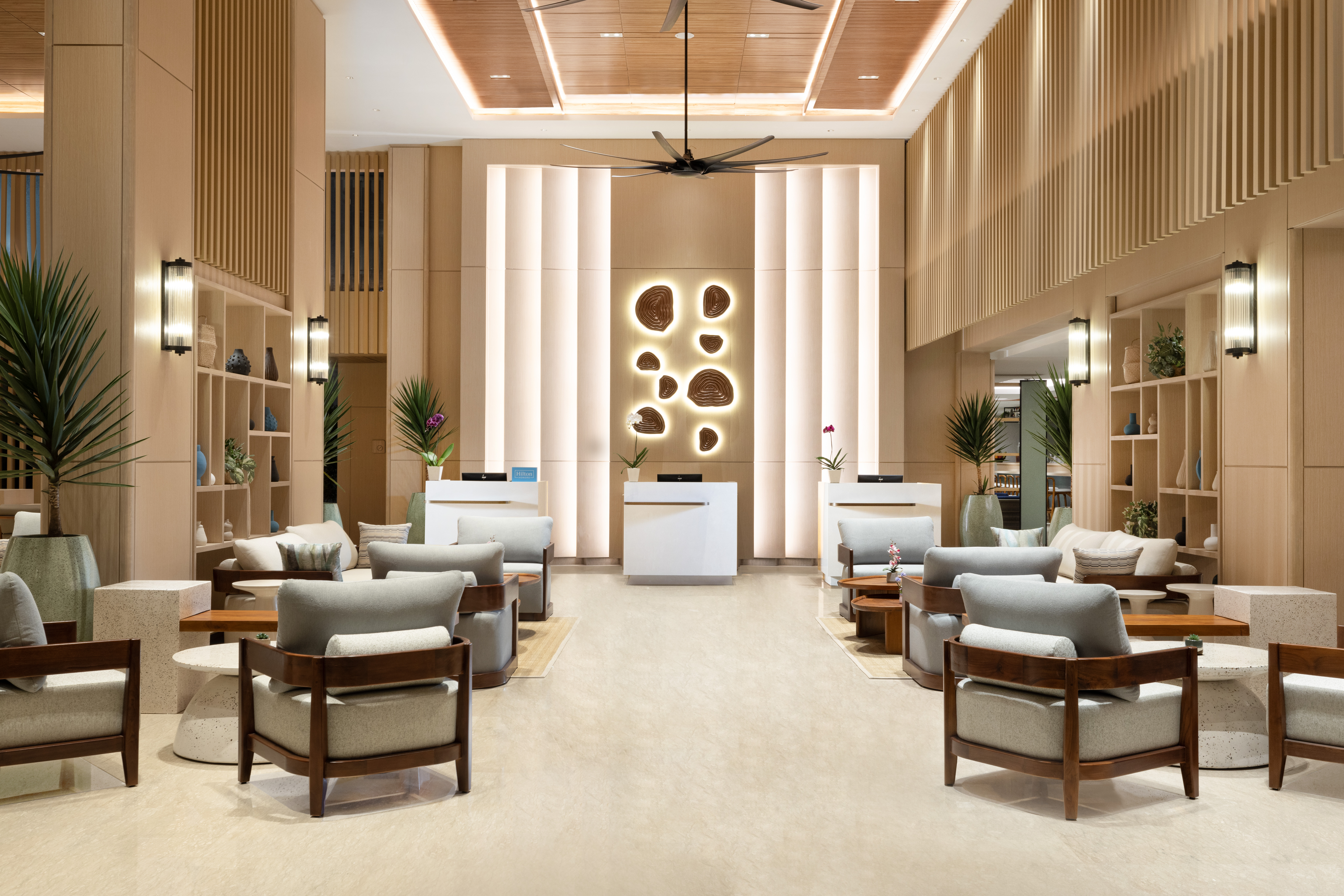 The bright and warm lobby of the Hilton Garden Inn Bali Nusa Dua with various seating areas framing the front desk.