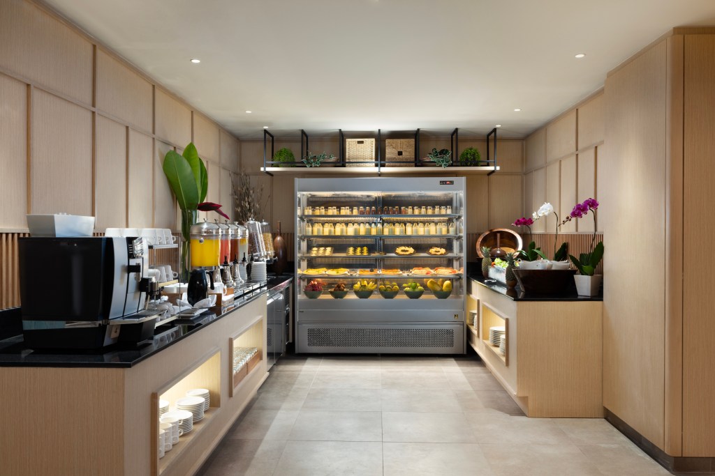 A section of the self serve portion of the restaurant with cold drink dispensers, coffee machine, and refrigerator with fruit