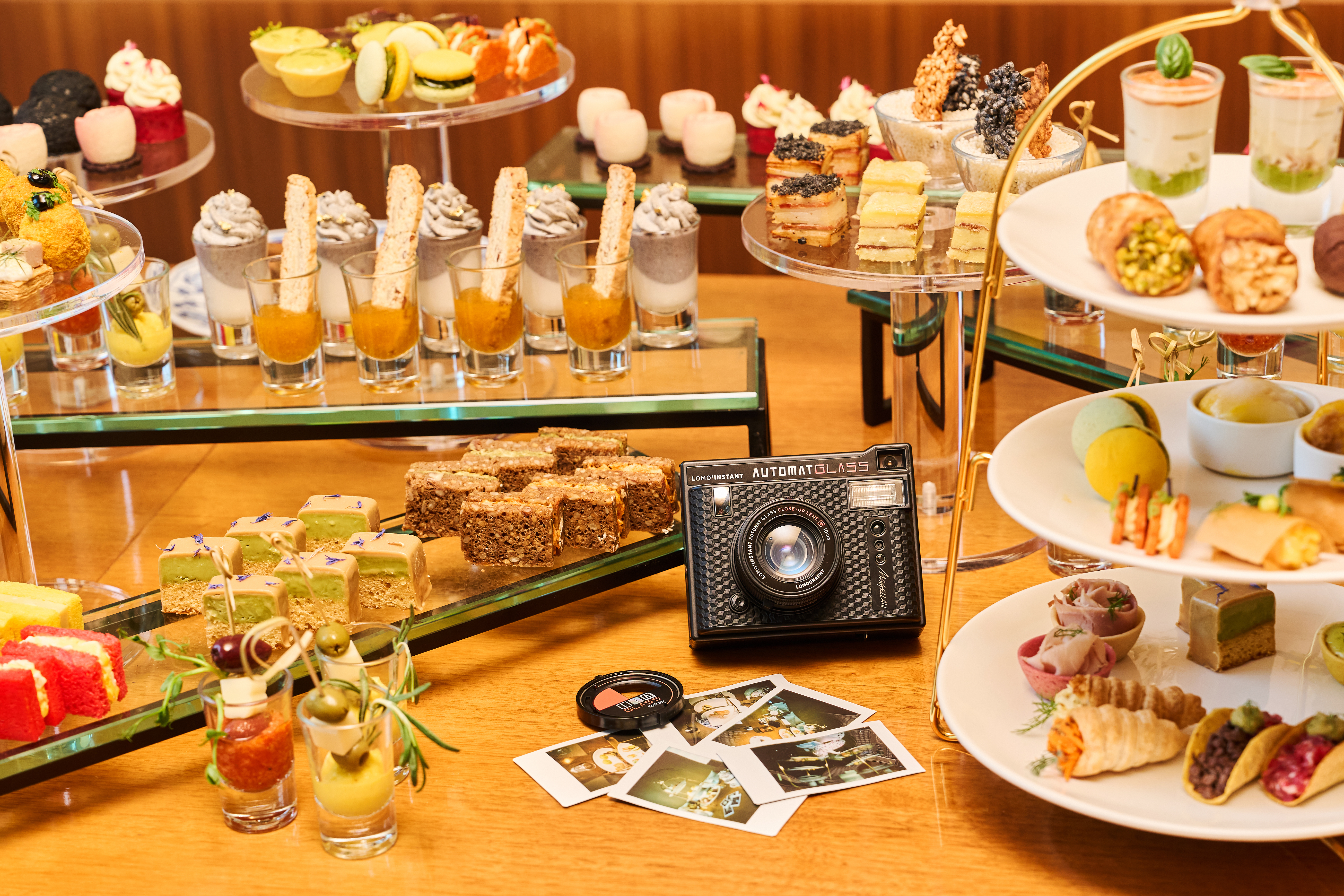 A camera surrounded by small sandwiches and desserts for a tea service