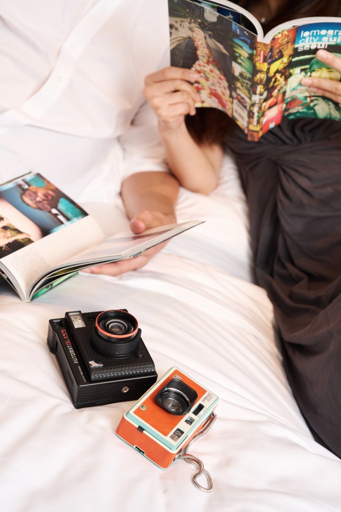 Two cameras on a bed between a couple looking at photography books.