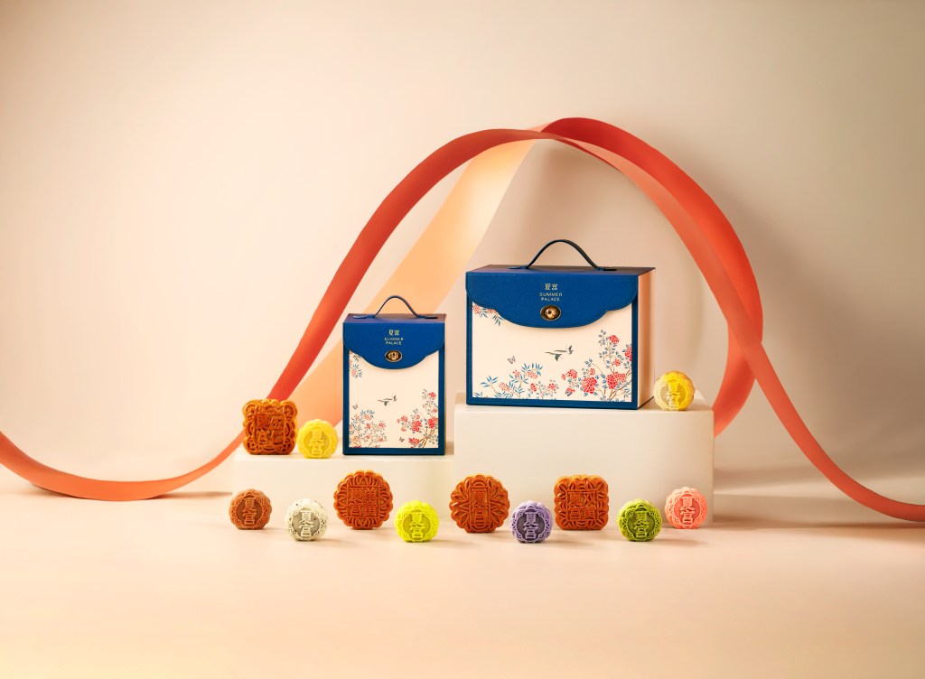 Colorful mooncakes in front of two briefcase shaped boxes with florals and birds.
