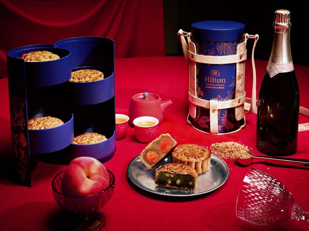 Mooncakes on a plate in front of two round boxes, one open, and one in a carrying case.