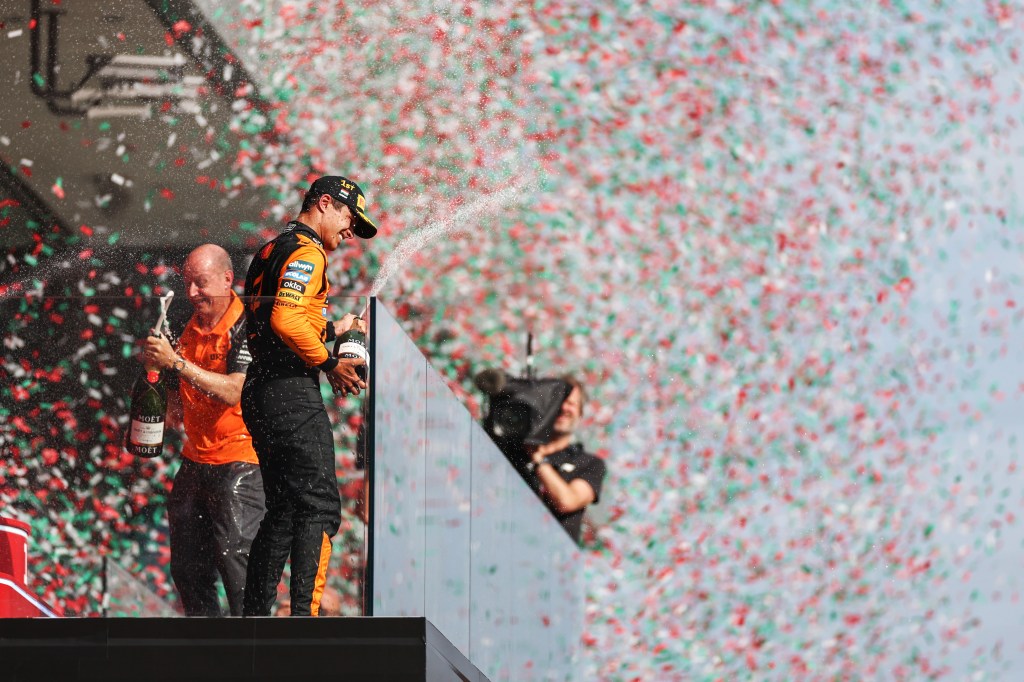Lando Norris celebrates with champagne on stage with confetti falling