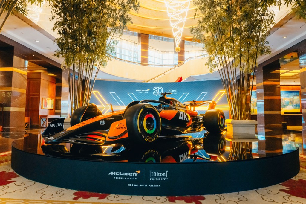 McLaren F1 Team car photo experience in the lobby of Conrad Singapore Marina Bay, car on a large circular black platform with McLaren Formula 1 Team Logo and Hilton. For The Stay Logo