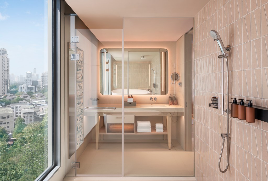 A hotel bathroom shot from inside the wet room, looking at the shower and a sink, with a bathtub behind