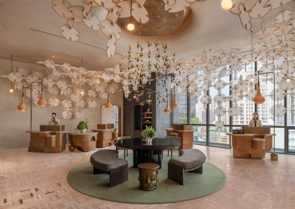 A lobby with a central table and benches, wooden front desks, and prominent sculpture hanging from the ceiling.
