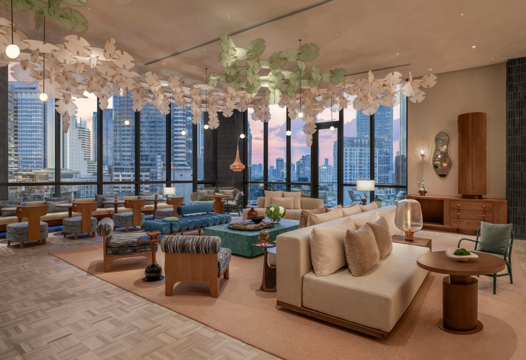 Many tables and chairs before large floor to ceiling windows overlooking the city.