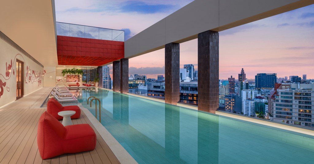 A pool on the roof top overlooking the city, with lounge chairs