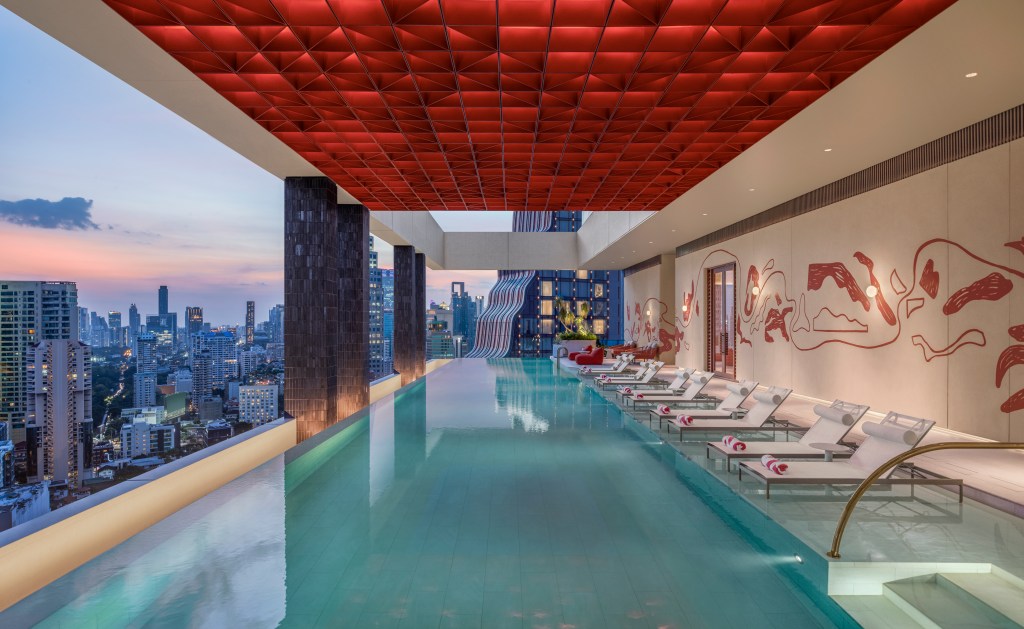A pool on the roof top overlooking the city, with lounge chairs