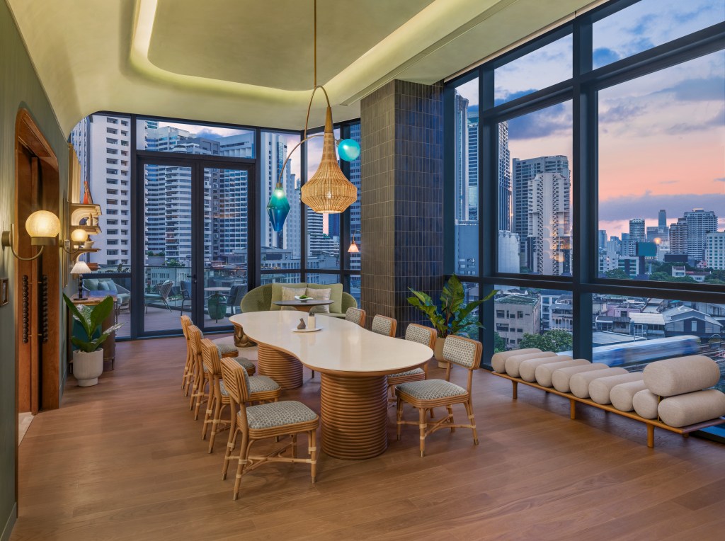 A peaceful space with table for eight and balcony behind, framed by a full wall of floor to ceiling window overlooking the city.