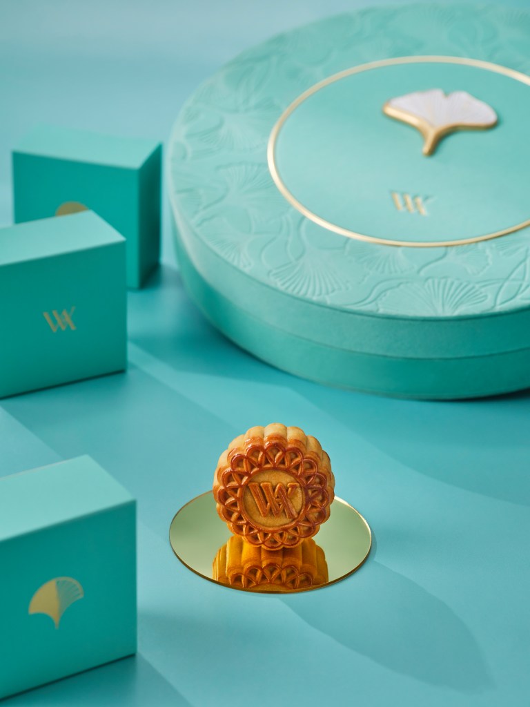A mooncake on a mirror in front of a light teal round box with floral engraving