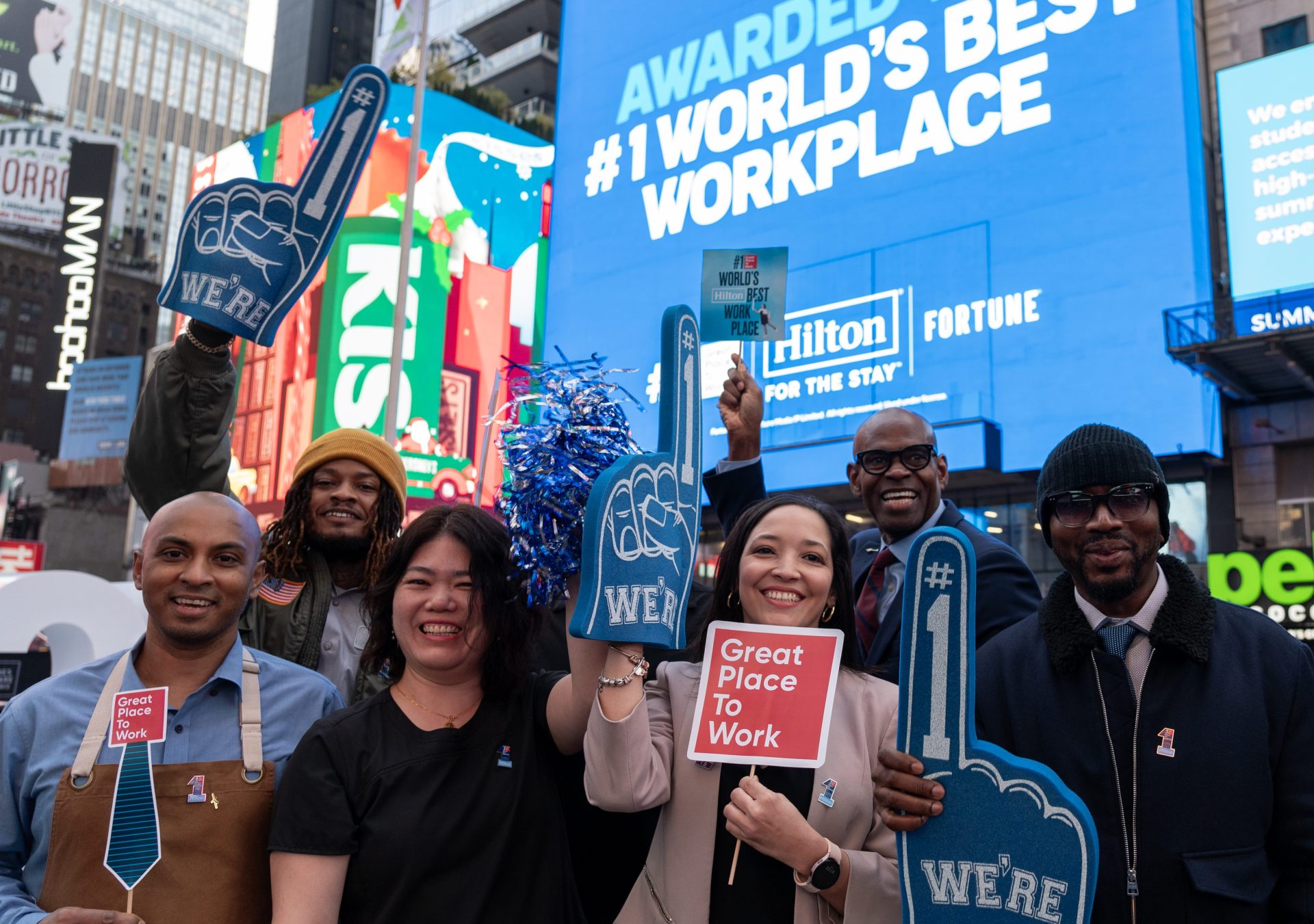 Group holding signs in front of Hilton #1 World's Best Work Place Screen in Times Square