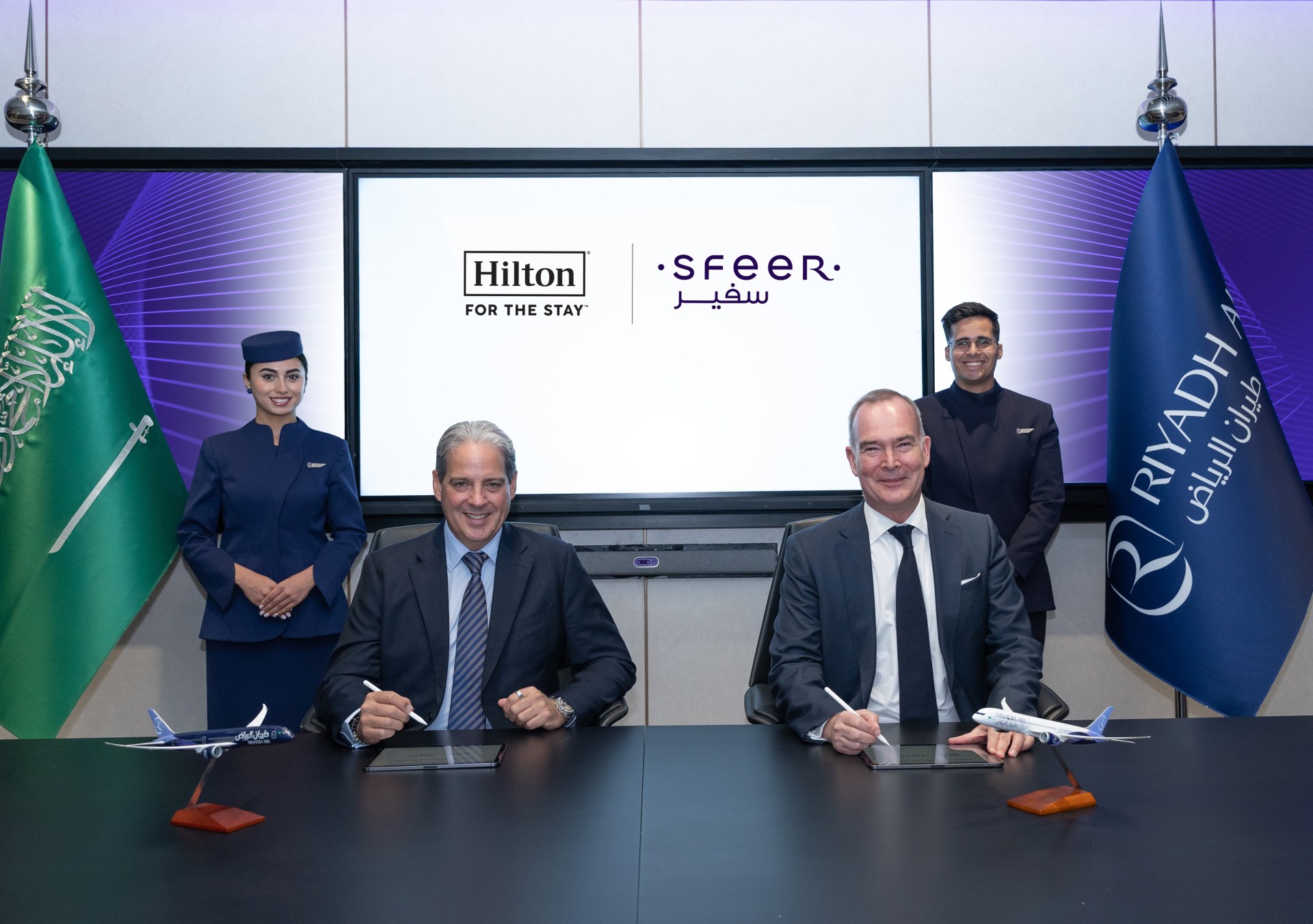 Executives sign papers while smiling at camera