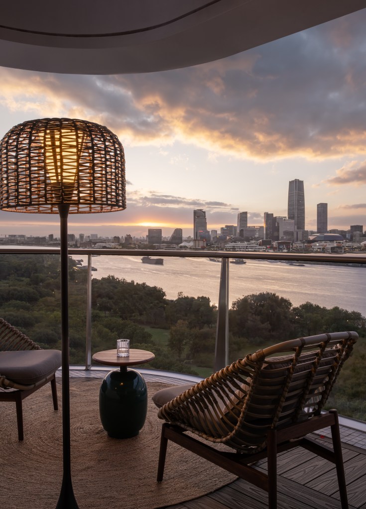 A balcony with small table and wicker chairs, looking out over the river and city