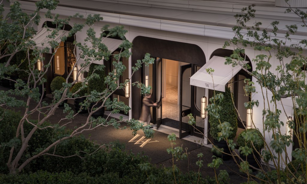 An entrance surrounded by bushes and trees, warmly lit at night, shot from above