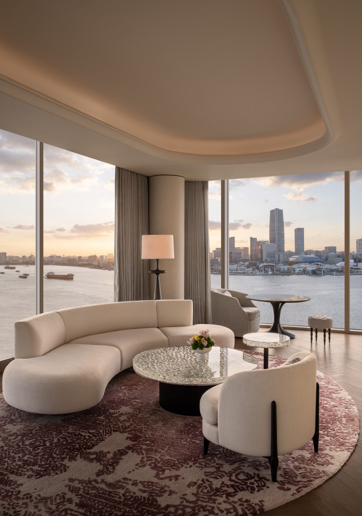 A seating area with couch and chair in front of large corner window looking out over the river and city