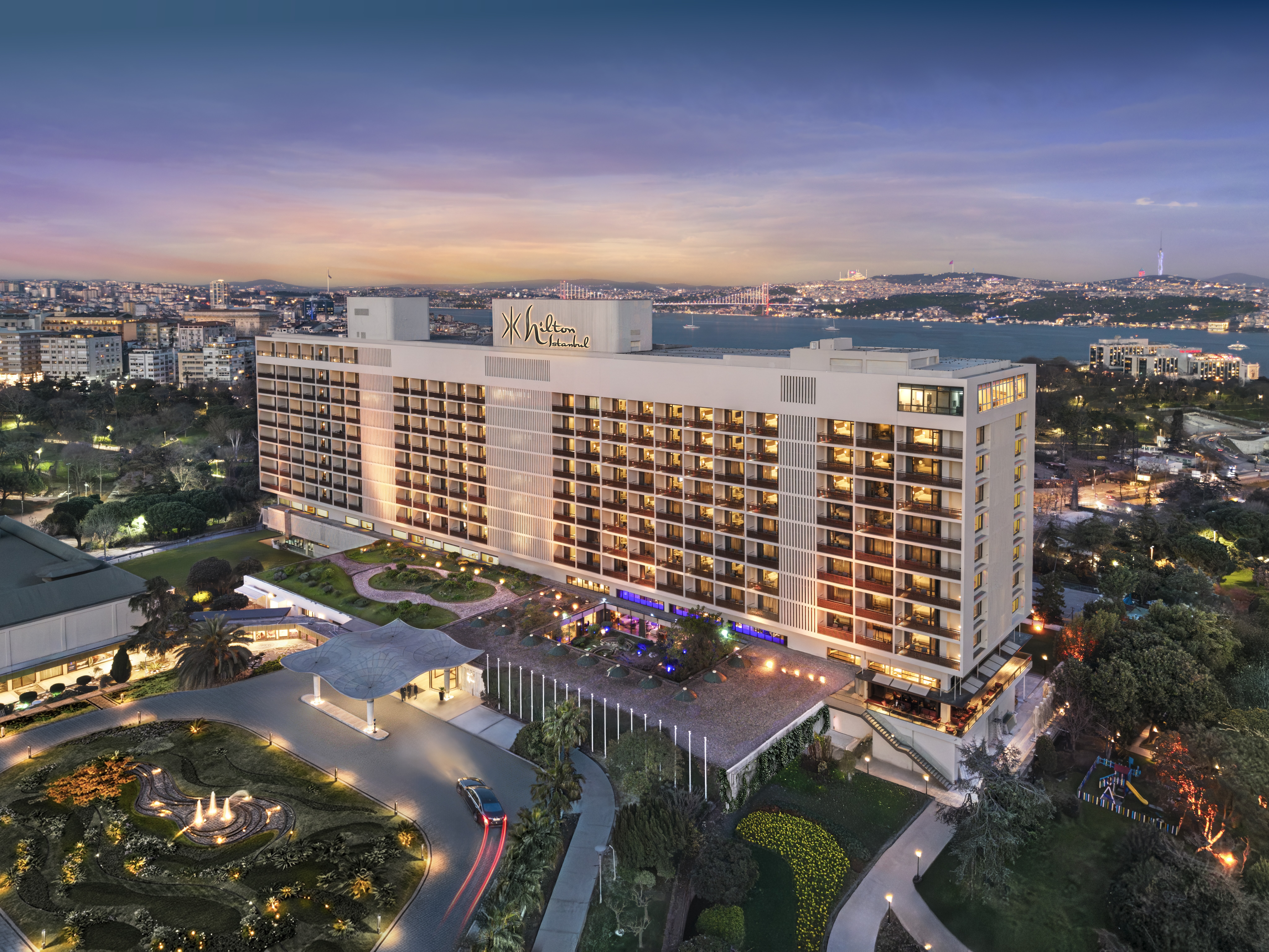 Hilton Istanbul Bosphorus hotel building illuminated at dusk with cityscape and water in the background.