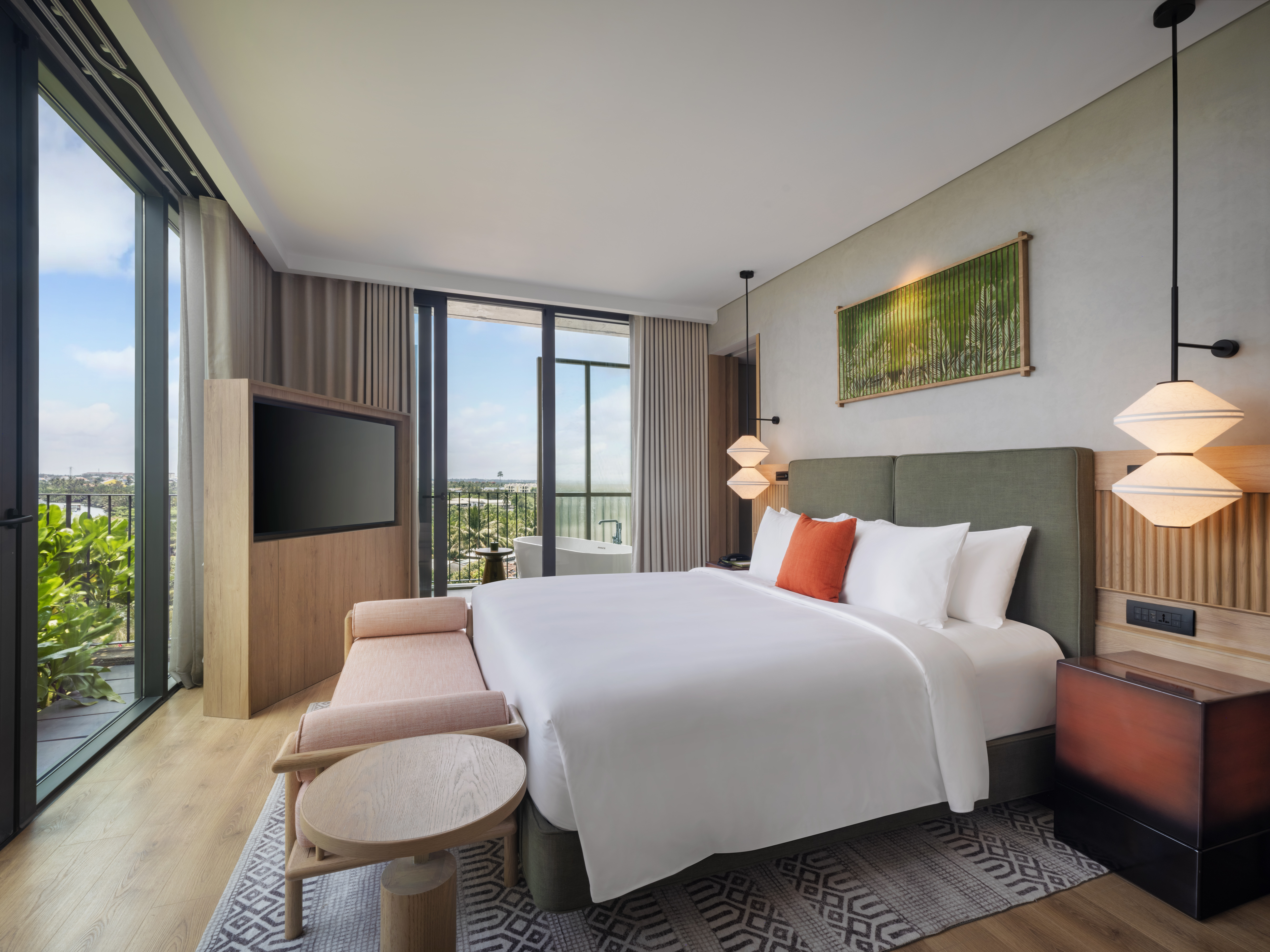 Modern hotel room at the NHAAN Resort & Spa Hoi An, Tapestry Collection by Hilton with a large bed, green upholstered headboard, hanging pendant lights, and a balcony with a view.