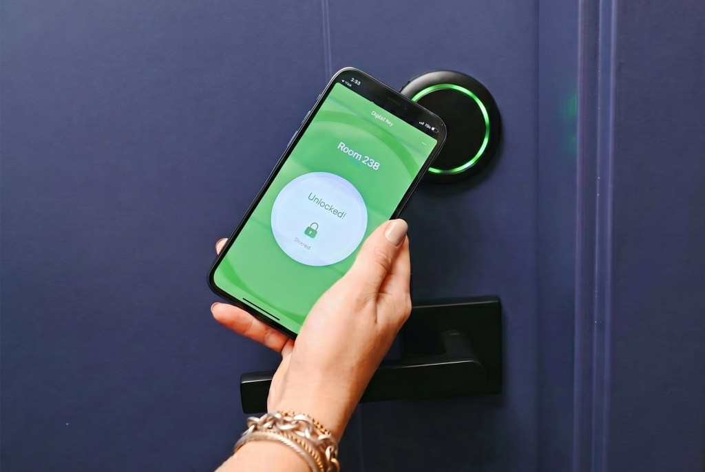 Hand holding a smartphone displaying a Hilton Honors App - Digital Key app showing "Room 238 Unlocked!" near a door lock with a green light.