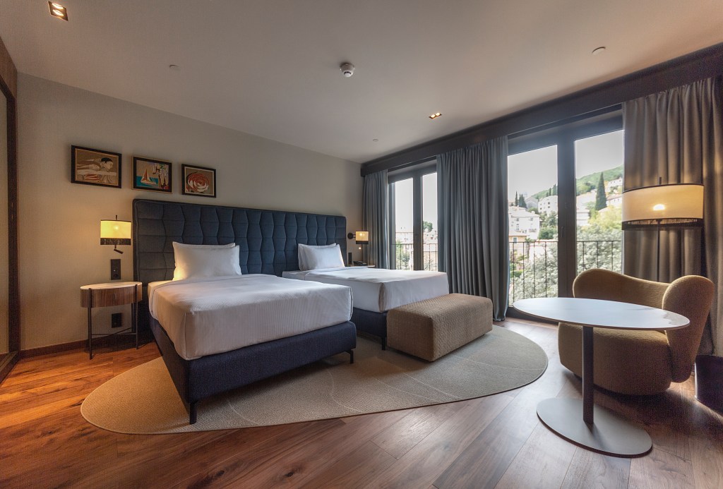 Guest Room with two twin beds, table and chair, large glass doors with view at Keight Hotel Opatija, Curio Collection by Hilton