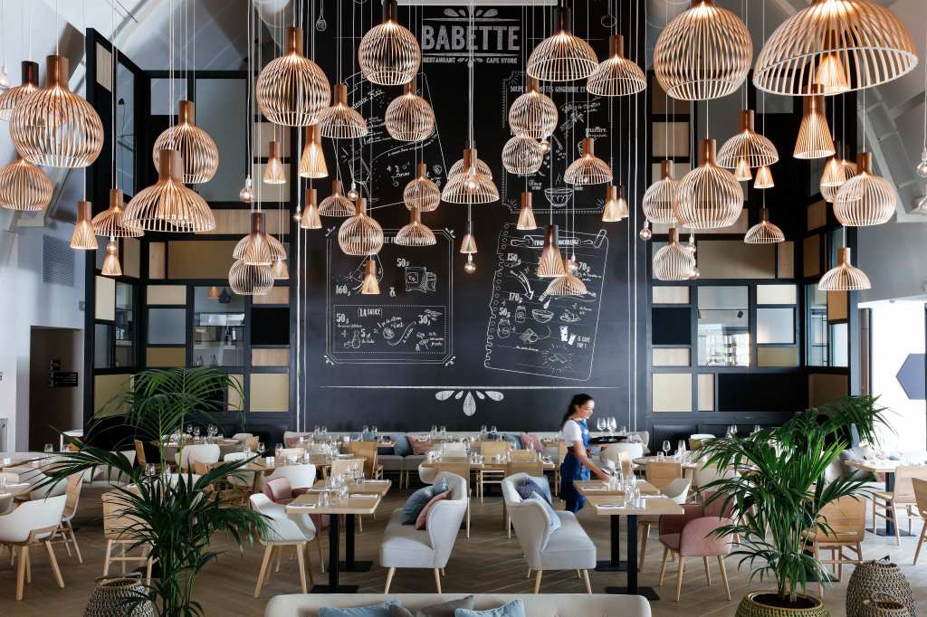 Hilton Garden Inn Paris La Villette - Babette restaurant seating area, tables, chairs with pillows, glasses, plants, wicker basket decor