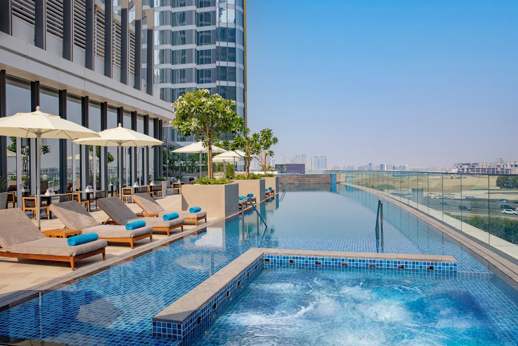 Embassy Suites by Hilton Dubai Business Bay - Pool - overlooking pool area with pool chairs, white umbrellas and trees in planters