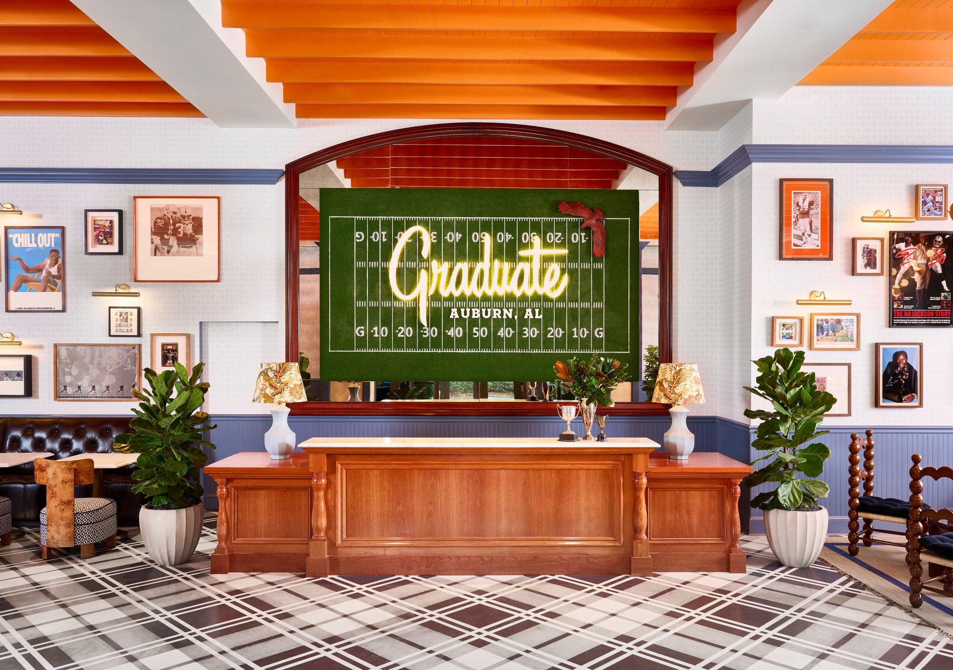 Graduate by Hilton Auburn AL - Lobby with check in desk featuring large football field art behind it, and walls with Auburn University artwork