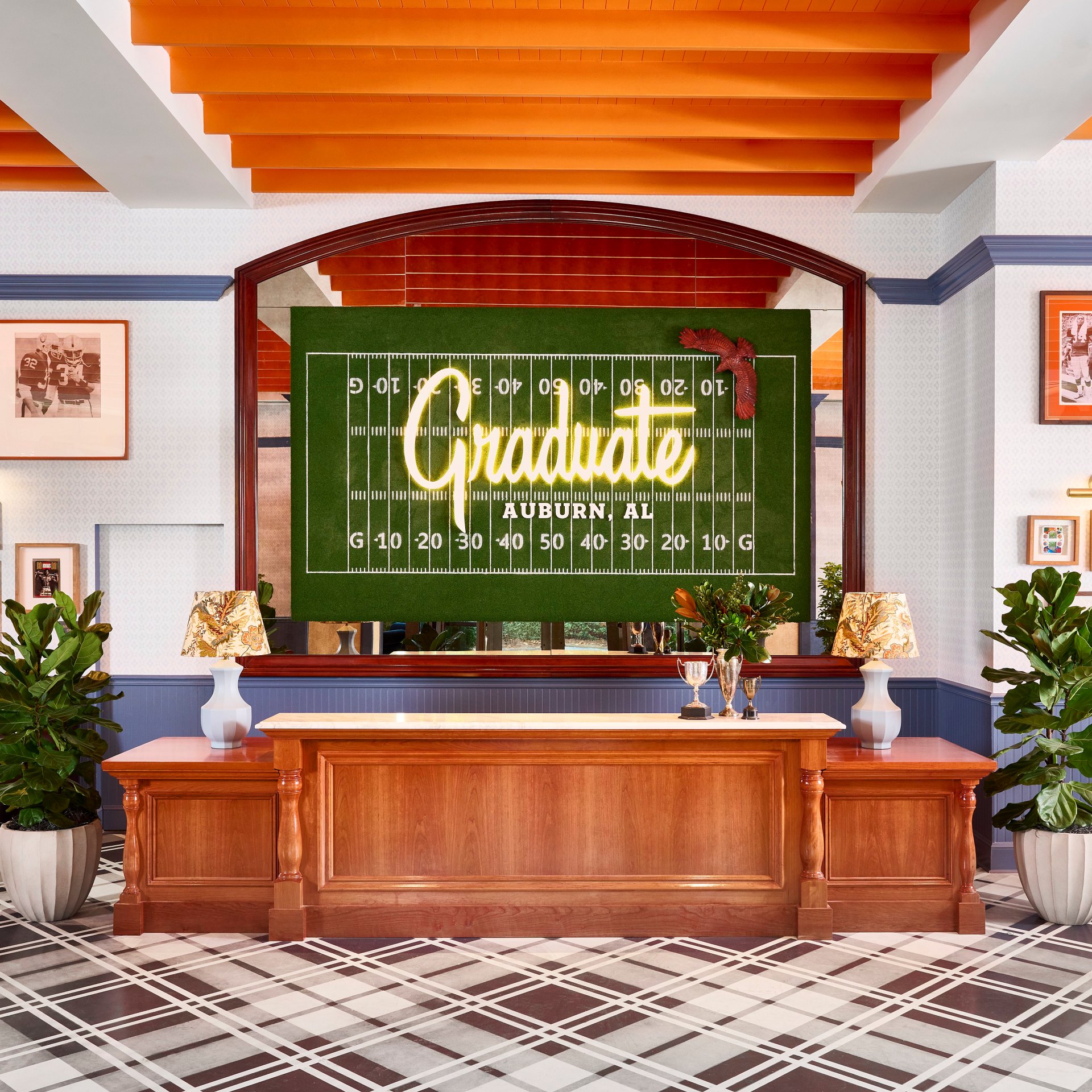 Graduate by Hilton Auburn AL - Lobby with check in desk featuring large football field art behind it, and walls with Auburn University artwork